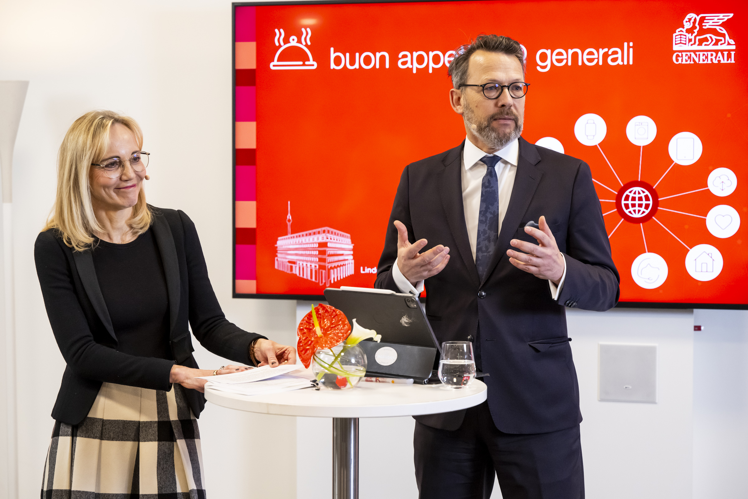 Dr. Timmesfeld und Herr Fricke stehen an einem Stehtisch und schauen ins Publikum. Im Hintergrund das Logo der Veranstaltung.